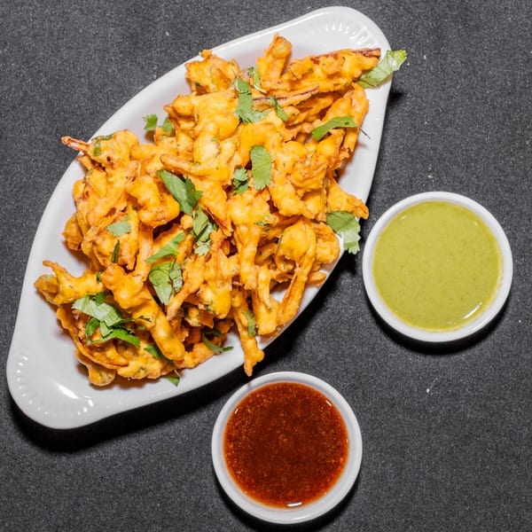 Crispy fried pakora, garnished with cilantro, served with green and red dipping sauces.