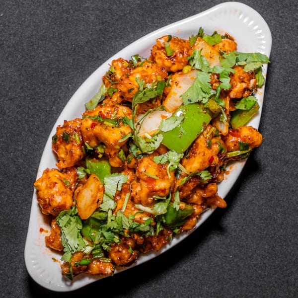 Spicy chili paneer with bell peppers, onions, and cilantro in a white dish on a dark background.